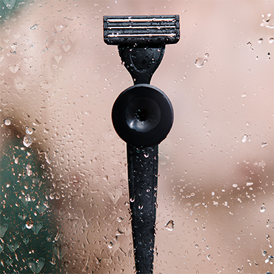 Schwarzer Rasierer haftet an nasser Duschwand, Glasoberfläche mit Wassertropfen bedeckt.