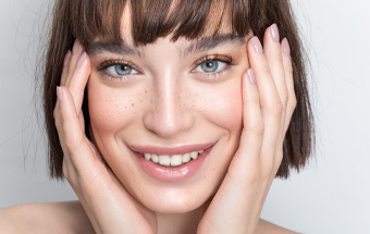 Person bedeckt das Gesicht mit den Händen – Beauty‑Look mit Fake‑Freckles und natürlichem Make‑up.