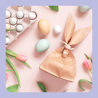 Oster-Dekoration mit pastellfarbenen Eiern, Tulpen und Papiertüte in Hasenform auf hellem Untergrund für frühlingshafte Inspiration.