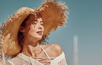 Person mit Strohhut am Strand – Tipps für gleichmäßigen Selbstbräuner und Sonnenschutz.