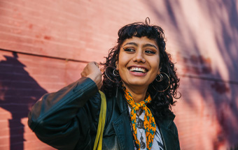 Person mit Locken, Lederjacke, gelbem Schal und Creolen vor Ziegelwand. Copyright: Getty Images