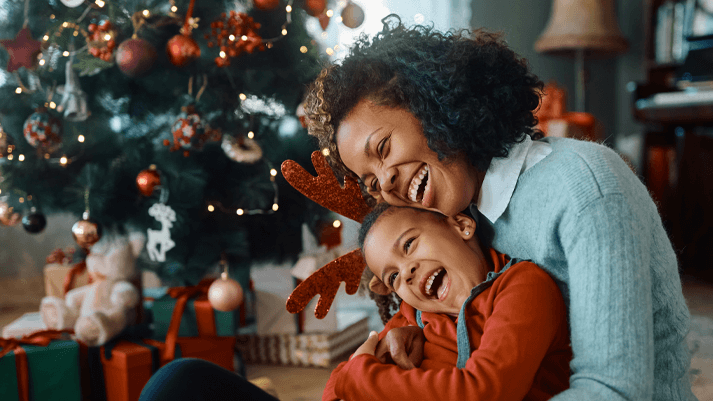 Frau umarmt Kind vor Weihnachtsbaum – emotionale Geschenkideen für Frauen zu Weihnachten