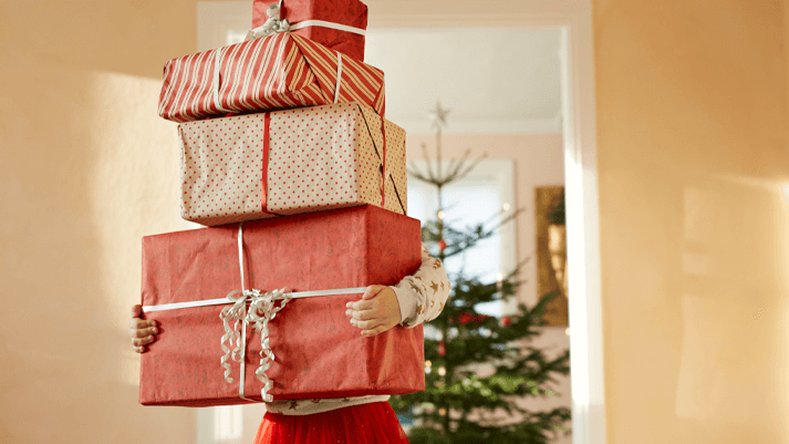 Person trägt Geschenke vor Weihnachtsbaum – festliche Stimmung, Weihnachten, Geschenkideen, Feiertage entdecken.