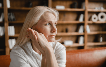 Person sitzt nachdenklich auf Sofa vor Bücherregal – mentale Gesundheit, Selbstreflexion, Ruhe, Menopause. Copyright: BIPA