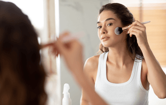 Person trägt Bronzer mit Pinsel vor Spiegel auf - Link zum Blogartikel Bronzer auftragen