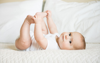 Baby spielt auf Bett – Hinweise zu Allergien und sanfter Hautpflege bei Babys.