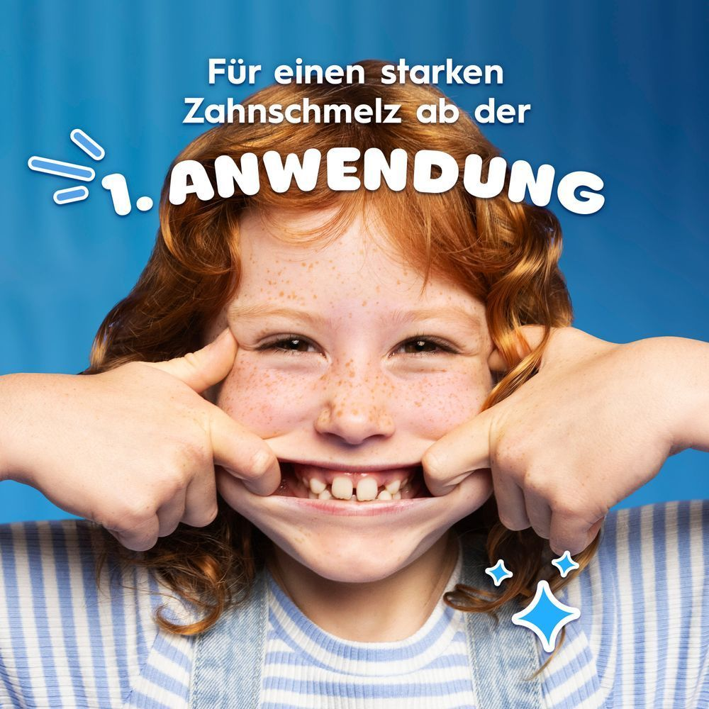 Mädchen mit gesundem Lächeln zeigt auf ihren Mund: Für starken Zahnschmelz ab der 1. Anwendung."