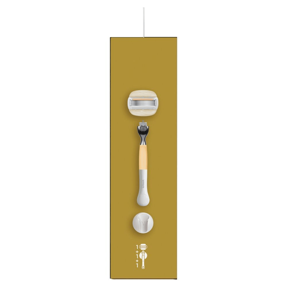 Venus Rasierer-Verpackung, die den Rasierer, eine Klinge, einen Duschaufhänger und eine zusätzliche Klinge zeigt. [IT] Gillette Venus rasoio con manico color oro, una testina di ricambio e supporto, confezionati in una scatola che indica 1+1+1. [ES] Venus ComfortGlide Special Edition en su caja mostrando una maquinilla y tres recambios.