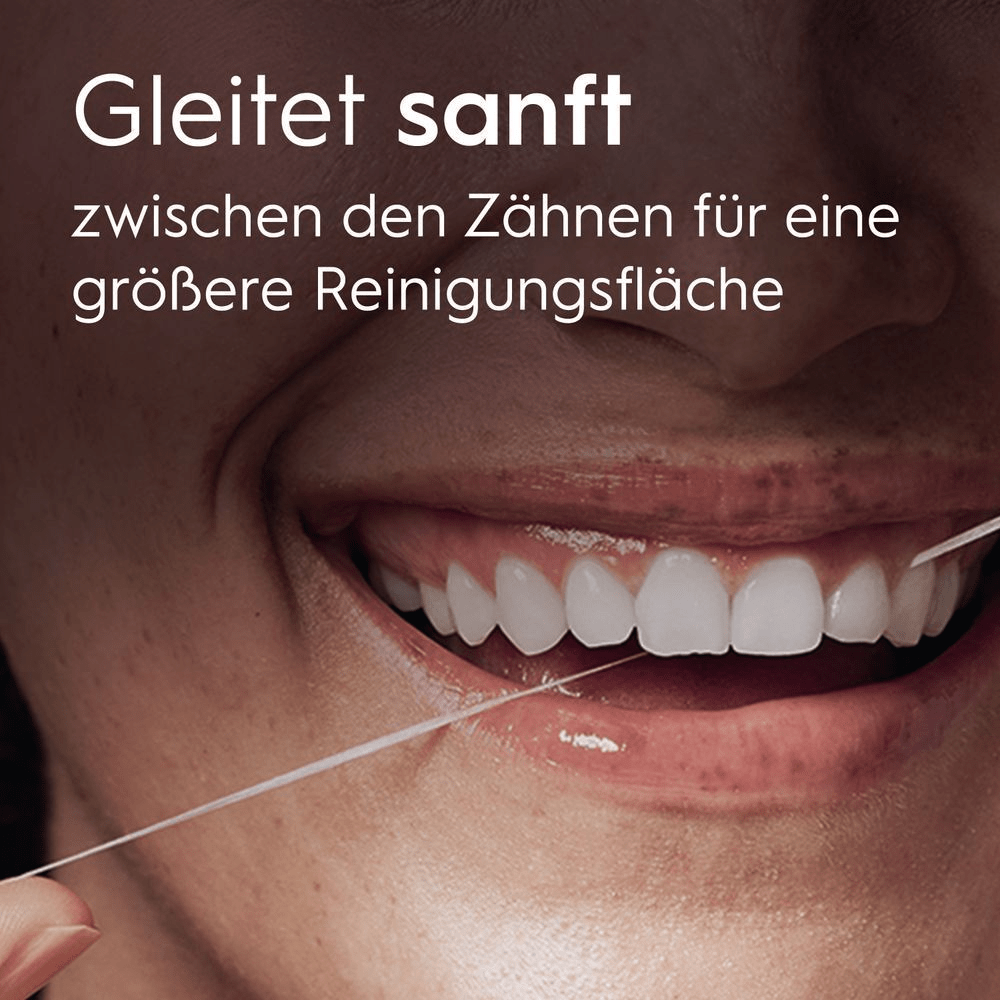 Nahaufname eines Mundes mit Zahnseide zwischen den Zähnen und um die Finger gewickelt.